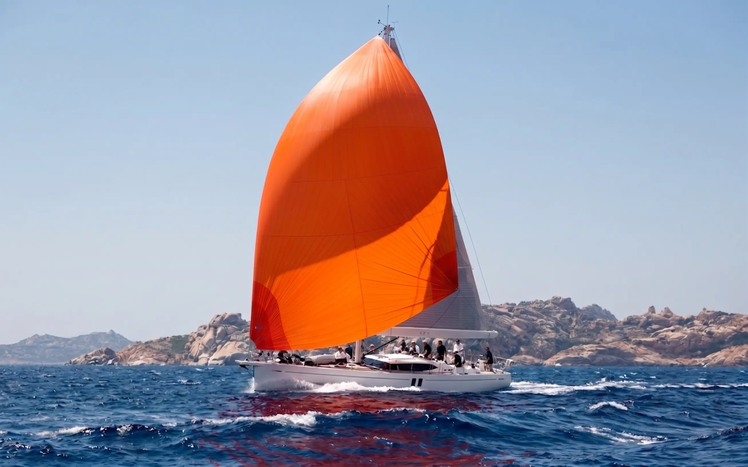A sailing yacht carrying a bright orange gennaker